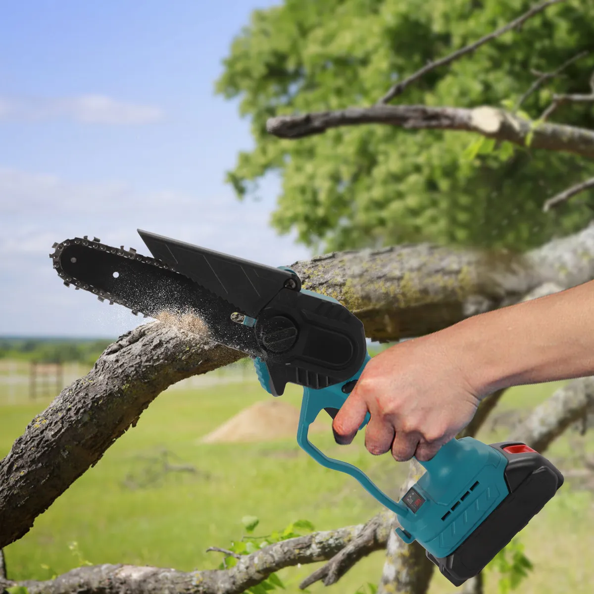 Élagage d'une branche à une main avec une mini-tronçonneuse sans fil, ciel bleu et prairie en arrière-plan